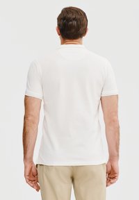 Biała koszulka polo z krótkim rękawem o klasycznym designie, z kołnierzykiem i delikatną fakturą. Widoczne szwy i gładka powierzchnia materiału.