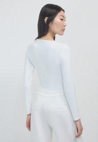 Haut blanc à manches longues avec un col rond, texture lisse et design ajusté, associé à un pantalon blanc taille haute avec des détails de couture subtils.