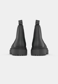 Bottines en cuir noir avec une semelle épaisse et robuste, et des languettes à l'arrière. Surface lisse et forme de bout arrondi.