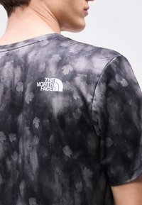 Άνδρας που φοράει μαύρο και γκρι μπλουζάκι τύπου tie-dye με διακριτικά φυτικά μοτίβα και λευκό λογότυπο The North Face στο πάνω μέρος της πλάτης.