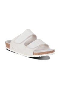 Sandales en suède gris clair avec deux sangles Velcro réglables, une semelle en liège et une semelle en caoutchouc blanc présentant un motif texturé.