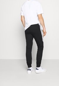 Černé tepláky se bílými bočními pruhy, tapered střih a elastické manžety, zkombinované s jednoduchým bílým tričkem a bílými teniskami.