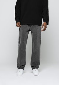 Baggy gray denim jeans with a subtle texture, paired with white sneakers. The outfit features a black long-sleeve shirt with text on the sleeve.
