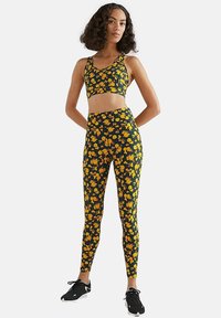 Sujetador deportivo negro con flores amarillas combinado con leggings de tiro alto a juego, que cuentan con un diseño ajustado y tejido elástico.