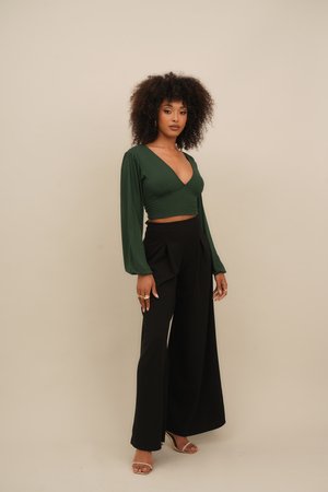 Green long-sleeve wrap top with a deep V-neck, paired with high-waisted black wide-leg trousers. Smooth fabric; model wearing clear heels.