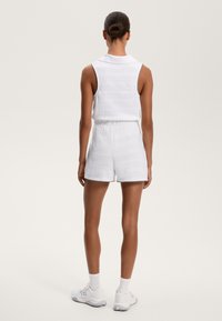 Witte mouwloze top met een kraag, gecombineerd met bijpassende shorts. Beiden hebben een gestructureerd patroon en zwarte stikaccenten. Witte sportschoenen.