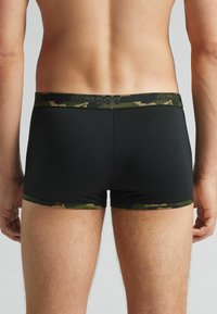 Boxer shorts negros con una cinturilla de camuflaje, hechos de un tejido elástico. Presentan un ajuste ceñido y una textura suave, ideales para la comodidad.