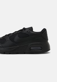 Chaussure de sport noire avec un mélange de cuir lisse et de maille respirante, bout arrondi, accents texturés et semelle avec amorti visible.