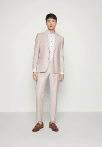 Light pink suit with a structured blazer and matching trousers, paired with a white dress shirt featuring black buttons, and brown loafers.