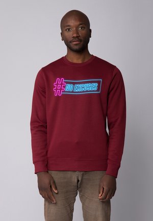 Burgunder Sweatshirt mit Rundhalsausschnitt, versehen mit einem neonfarbenen Grafikdesign mit dem Text "#NO EXCUSES" in Blau und Pink, strukturierter Stoff, lange Ärmel.