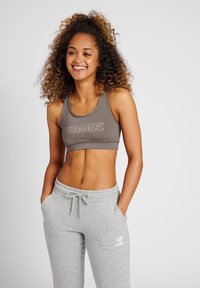 Szary stanik sportowy z logo "HUMMEL", w połączeniu z jasnoszarymi dresami z białym logo. Materiał wydaje się gładki i elastyczny.