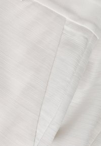 Detailní záběr na bílou strukturovanou tkaninu s diagonálními švy a jemným žebrovaným vzorem.