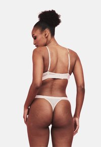 Set di lingerie rosa chiaro composto da un reggiseno a spalline sottili con chiusura a gancio e un perizoma abbinato dal design minimalista e con elastico.