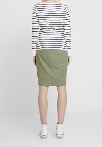 Outfit da donna composto da una maglietta a maniche lunghe a righe black e white, una gonna verde al ginocchio e sneakers bianche alte.