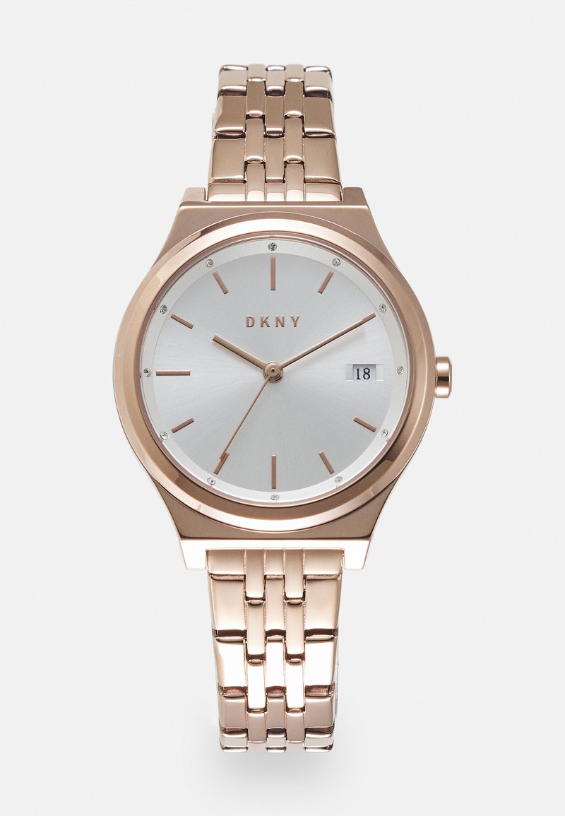 Roze gouden DKNY-horloge met een zilveren wijzerplaat, minimalistische uurmarkeringen en kristalaccenten. Beschikt over een metalen schakelarmband en een datumaanduiding.