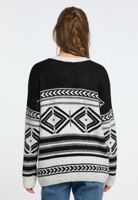 Schwarzer und weißer gemusterter übergroßer Pullover mit geometrischen Designs und dicker Stricktextur, versehen mit einem Rundhalsausschnitt und überschnittenen Schultern.