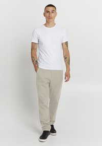 Weißes Kurzarm-T-Shirt kombiniert mit beigen Hosen und schwarzen Sneakers. Das Outfit zeichnet sich durch ein schlichtes, lässiges Design mit figurbetontem Schnitt aus.