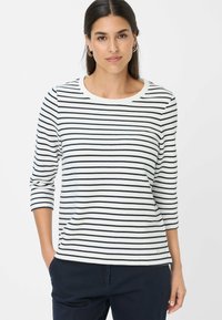 Langarmshirt mit rundem Halsausschnitt in Weiß mit marineblauen horizontalen Streifen. Es hat eine lockere Passform und bietet ein kleines Akzentdetail am Saum.