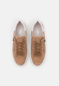 Baskets avec une extérieure en suède marron clair, col rembourré, partie avant à lacets marron, et fermeture éclair latérale. Semelle en caoutchouc blanche, design minimaliste.