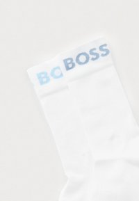 Białe bawełniane skarpetki o miękkiej fakturze, z jasnoniebieskim logo "BOSS" na mankiecie. Projekt jest prosty i klasyczny.