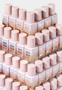 Revolution Skin Silk-flasker arrangert i en pyramide, med frostet rosa glass, runde hetter og gullfarget etikettdekorasjon.