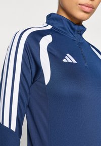 Ναυτικό μ πλε αθλητικό πουκάμισο με φερμουάρ, με λευκές ρίγες στο πλάι, υφή υφάσματος, ψηλό γιακά και το λογότυπο της Adidas στο στήθος.