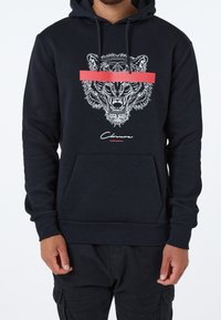 Sudadera negra con capucha que presenta un gráfico de la cabeza de un león en blanco con una franja horizontal roja. Incluye un bolsillo frontal y puños acanalados.