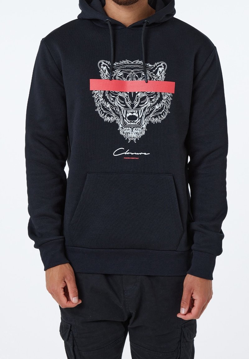 Sudadera negra con capucha que presenta un gráfico de la cabeza de un león en blanco con una franja horizontal roja. Incluye un bolsillo frontal y puños acanalados.