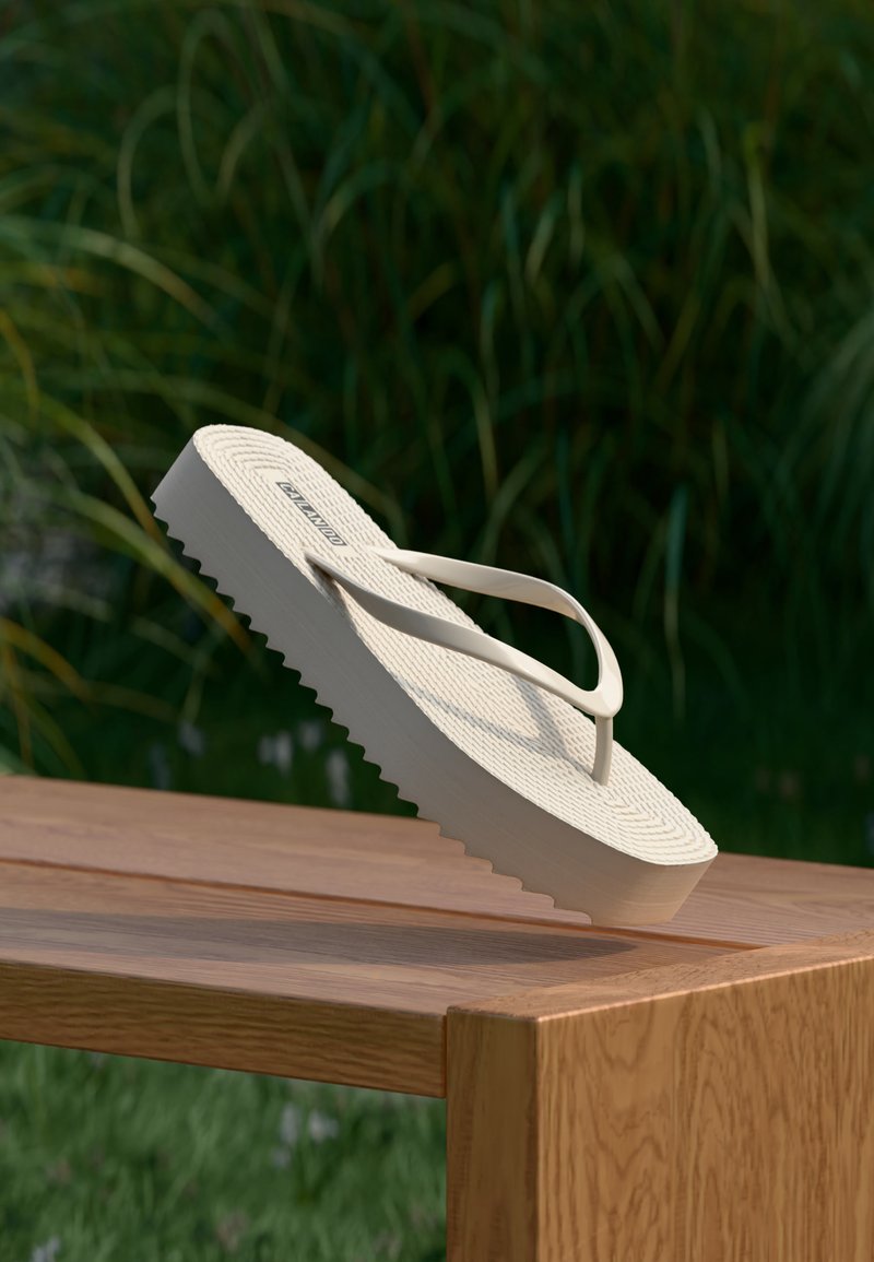 Tongs à plateforme beige inclinées sur le bord d'une table en bois avec des plantes vertes floues en arrière-plan.