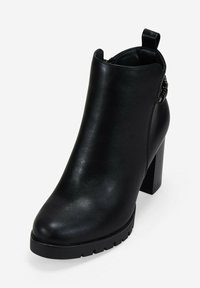 Botín negro de cuero hasta el tobillo con tacón cuadrado, cremallera lateral, tirador y suela resistente.