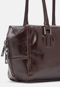 Czarna, błyszcząca skórzana torebka z podwójnymi uchwytami, widocznym szwem, boczną kieszenią na zamek błyskawiczny oraz srebrnymi uchwytami zamka na białym tle.