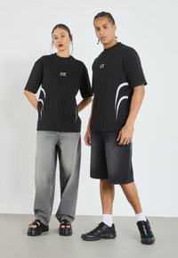 Svarta t-shirts med vita grafiska detaljer, grå baggy jeans och svarta shorts. Skor inkluderar platåsandaler och eleganta sportskor.