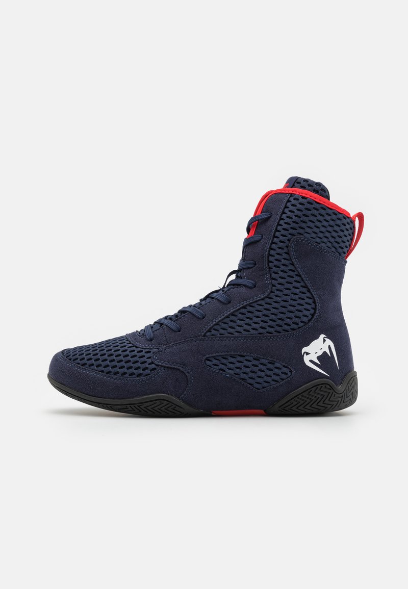 High-top athletic shoes in navy suede with mesh panels, red accents on the collar and laces, and a black rubber outsole with a logo detail.