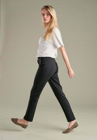 Čierne nohavice na mieru so slim fit strihom, skombinované s svetlo šedým topom s krátkym rukávom. Model má na sebe hnedé ploché topánky.