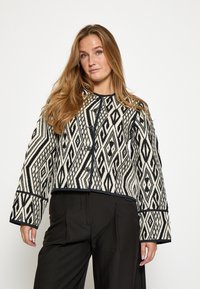 Woven cropped jacket with a black and white geometric pattern, featuring a round neckline, long sleeves, and front button closure.