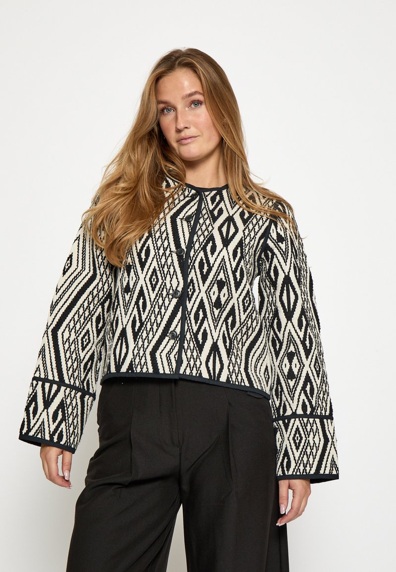 Woven cropped jacket with a black and white geometric pattern, featuring a round neckline, long sleeves, and front button closure.