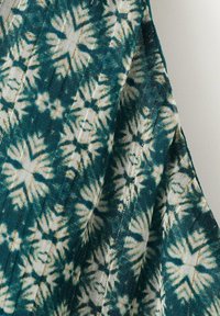 Niebiesko-biała tkanina farbowana metodą tie-dye z symetrycznym wzorem promienistym, ułożona tak, aby ukazać fakturę i fałdy.