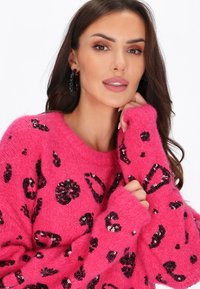 Różowy sweter z dzianiny, pokryty czarnymi cekinami w kształcie lamparcich plam, z okrągłym dekoltem i długimi rękawami z lekko oversize'owymi mankietami.