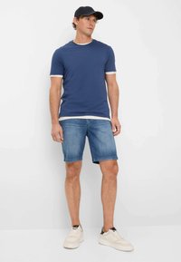 T-shirt blu navy con bordo bianco, abbinata a pantaloni corti in denim azzurro e sneaker bianchi. Design minimalista e vestibilità casual.