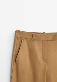 Benvita högmidjade byxor med två sidofickor, som har ett slätt tyg och fina veck fram, visade mot en enfärgad vit bakgrund.