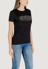 T-shirt nera in cotone con maniche corte, caratterizzata da un design logo in strass scintillanti sulla parte anteriore e un classico collo a giro.