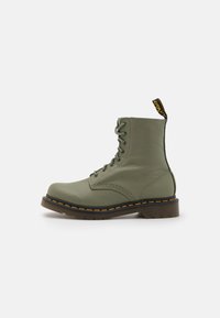 Des bottes en cuir vert à lacets présentent un bout rond, une hauteur cheville et une semelle en caoutchouc épaisse avec des coutures jaunes et une languette.
