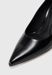 Scarpa nera con tacco alto e punta affilata, realizzata in pelle liscia. L'interno presenta una finitura elegante e lucida. Nessun hardware o accenti visibili.