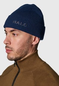 Niebieska dziergana czapka z prążkowaną fakturą i podwiniętym mankietem, z wyhaftowanym napisem "HALO" w jasnobrązowej nici.