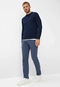 Pull en maille marine à manches longues, associé à un pantalon chino bleu et des baskets blanches. Design simple, texture douce et palette de couleurs neutres.
