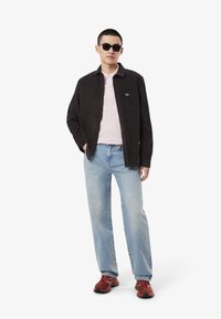 Svart kordflorsskjorta, ljusrosa polo, ljus tvättade lösa jeans, röda och svarta sneakers, runda solglasögon. Diskret logotyp på skjortan.