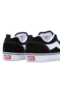 Paire de baskets Vans noires et blanches vues de dos, avec coutures blanches et logo rouge "Vans Off The Wall" sur les semelles.