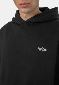 Black hoodie made of soft fabric featuring a kangaroo pocket, ribbed cuffs, and a small white logo on the chest. Simple and minimalist design.