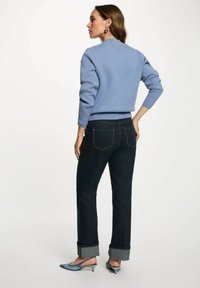 Maglione azzurro chiaro con polsini a coste, abbinato a jeans in denim scuro con orli arrotolati. Scarpe con tacco nere e blu.