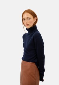  granatowy sweter z golfem wykonany z miękkiego materiału, z długimi rękawami i dopasowanym krojem. Połączony z brązową skórzaną spódnicą o gładkiej fakturze.